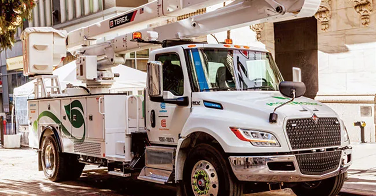 A white commercial utility work truck equipped with a Terex bucket lift parked on a city street, showcasing green sustainability branding on the door.